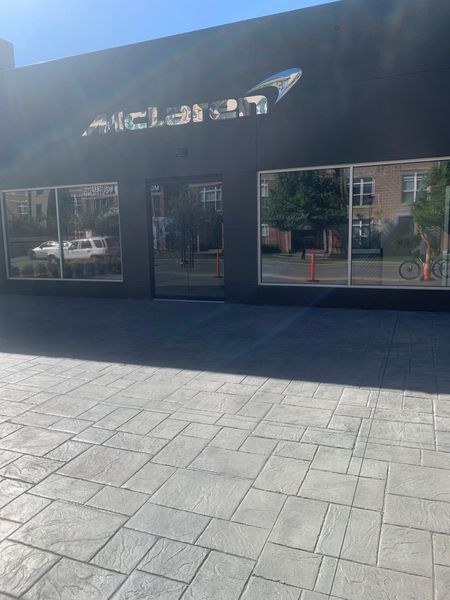 The exterior of a McLaren showroom featuring a black facade, large glass windows, and a paved stone courtyard.