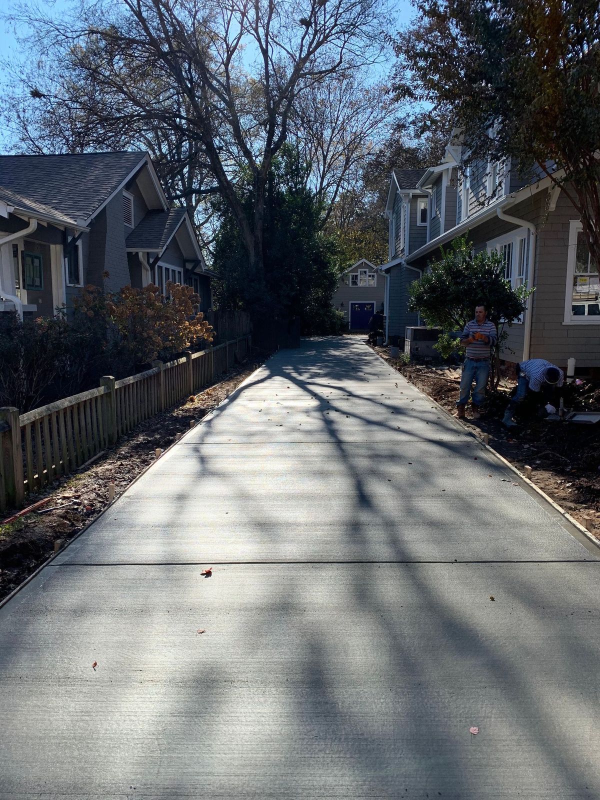 A newly paved concrete driveway stretching between two houses with a person working on the side.