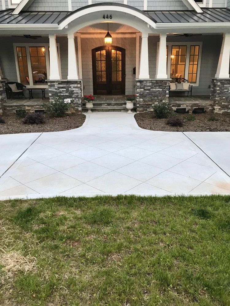 A view of a house exterior with a gray, diamond-patterned concrete walkway leading to a covered front porch and entry.