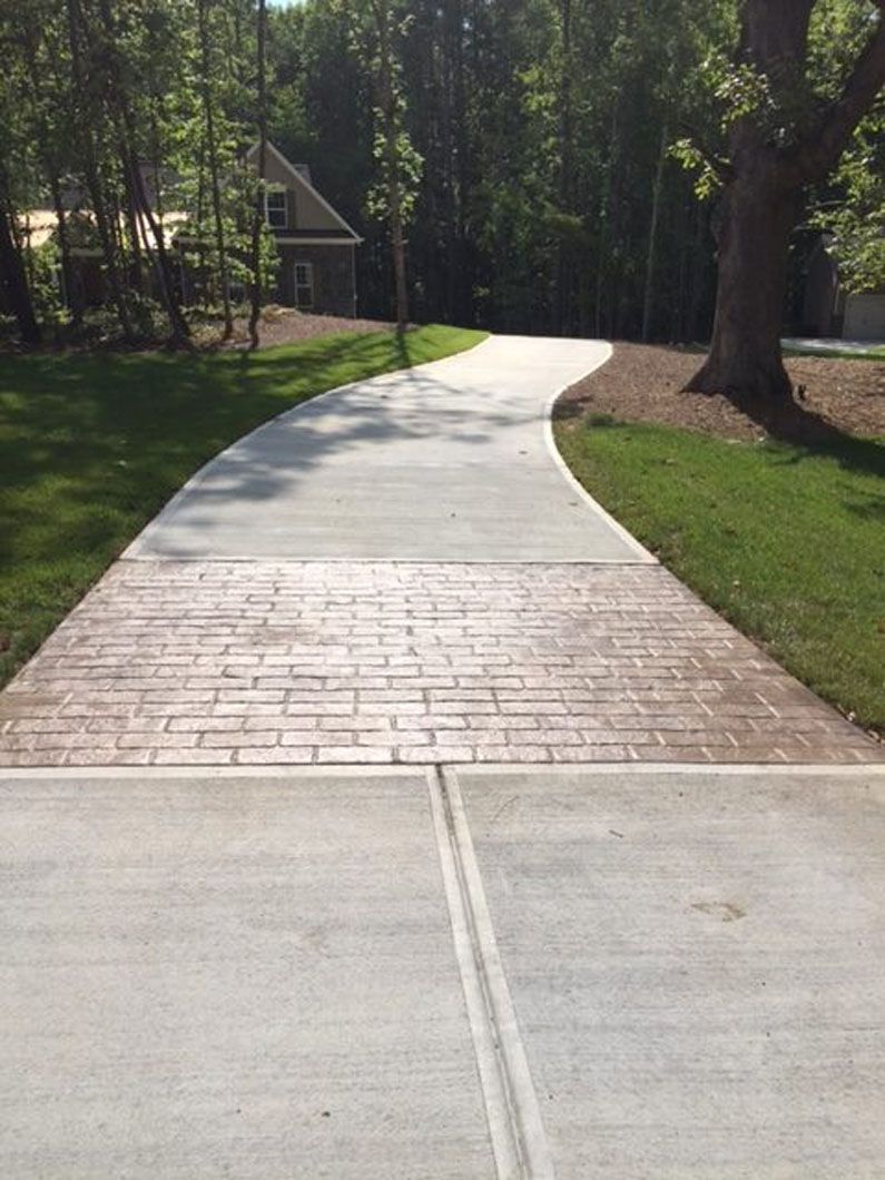 A concrete driveway transitions from a smooth gray section to a brown, brick-patterned stamped concrete section.