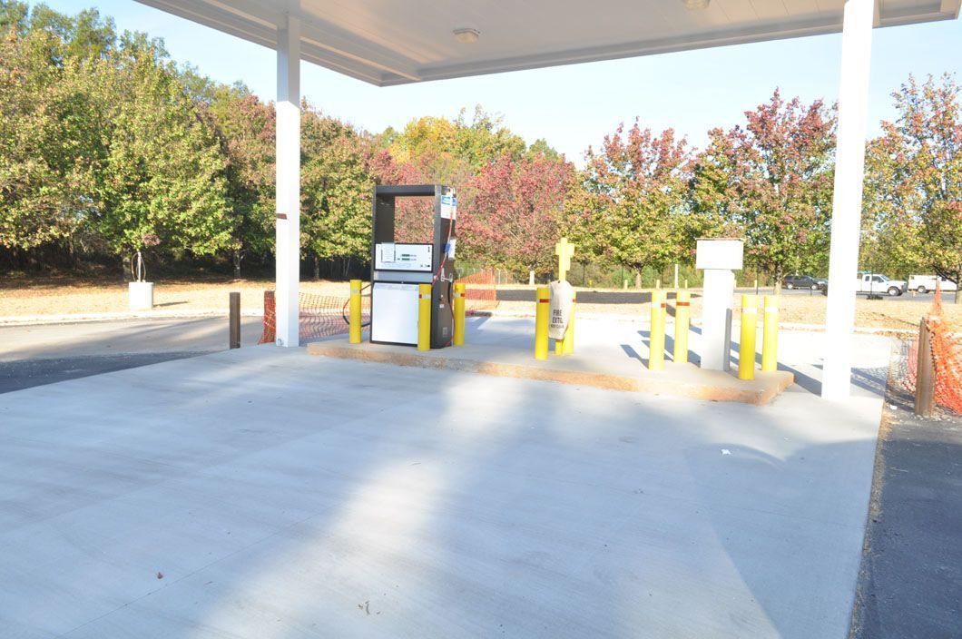 A newly paved gas station island with two fuel pumps under a canopy, surrounded by yellow safety bollards.