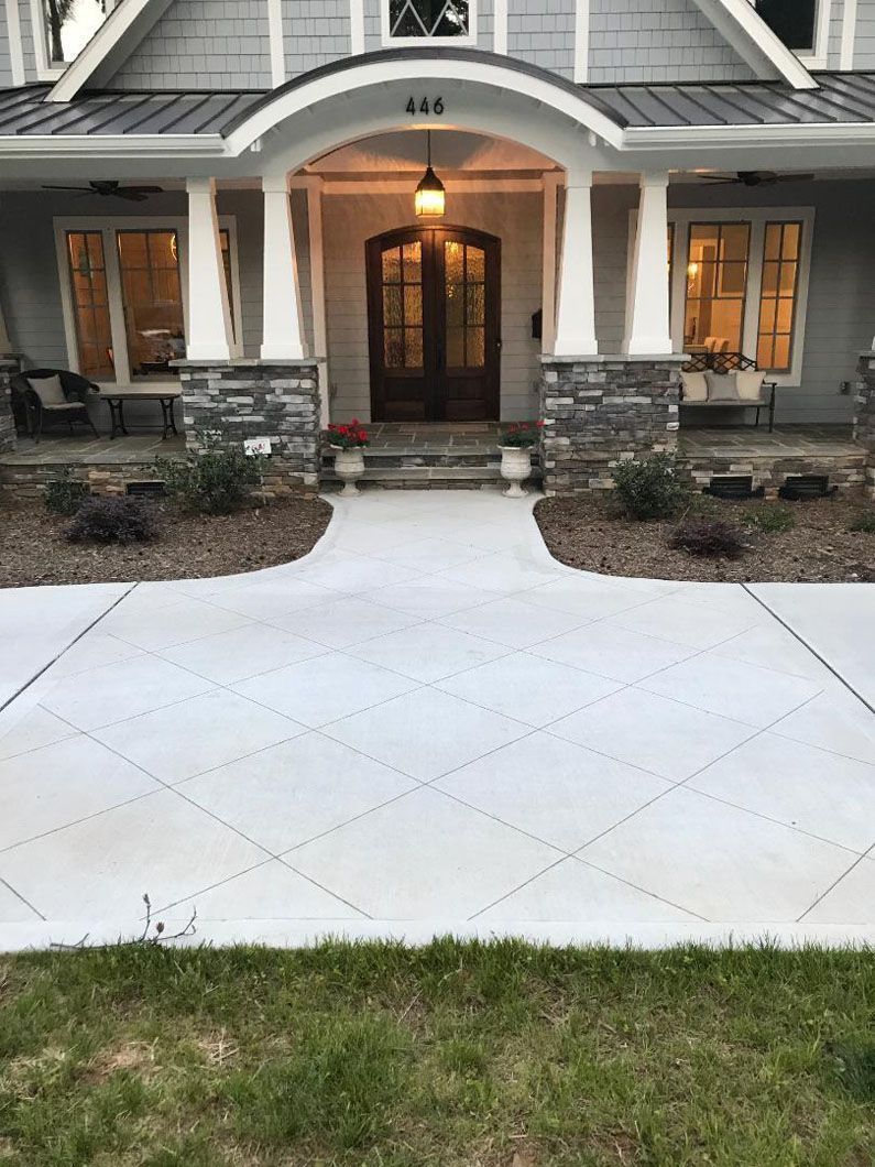 A front-facing view of a gray house with a stone porch, a concrete walkway with a diamond pattern, and a wooden front door.