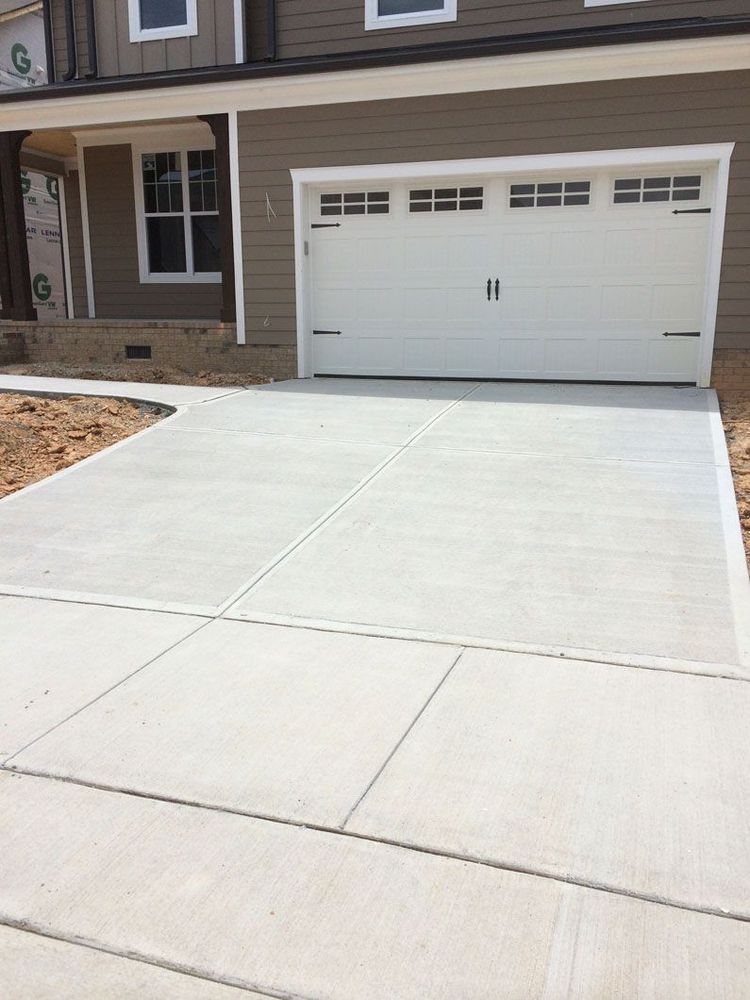 A tan, multi-story house with a white garage door and a freshly poured light gray concrete driveway.