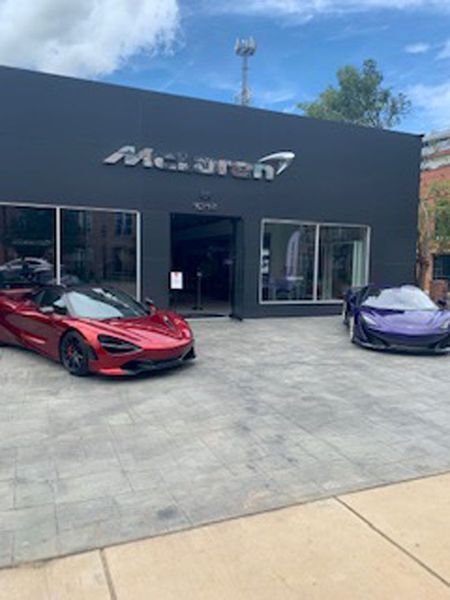 A McLaren dealership with a metallic red car parked on the left and a purple sports car on the right.