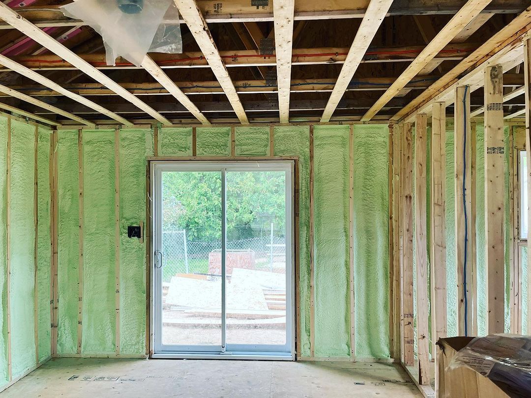 Interior of a room under construction, green insulation on walls, sliding glass door, exposed wooden beams.