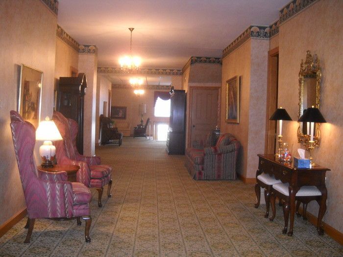 Hallway with antique furniture, lamps, and framed art. The floor is tiled, and the walls are textured.