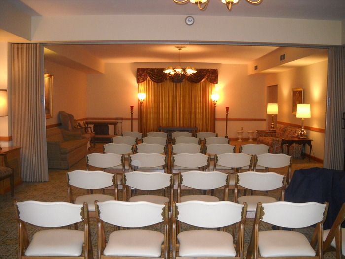 Rows of chairs face a stage with gold curtain in a quiet funeral home.