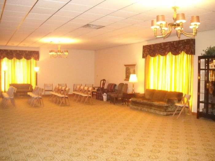 Empty room with couches, chairs, and a chandelier, possibly a funeral home.