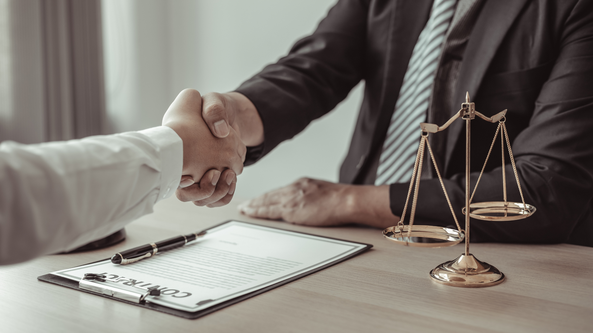 Two people shaking hands over a contract, scales of justice on the table.