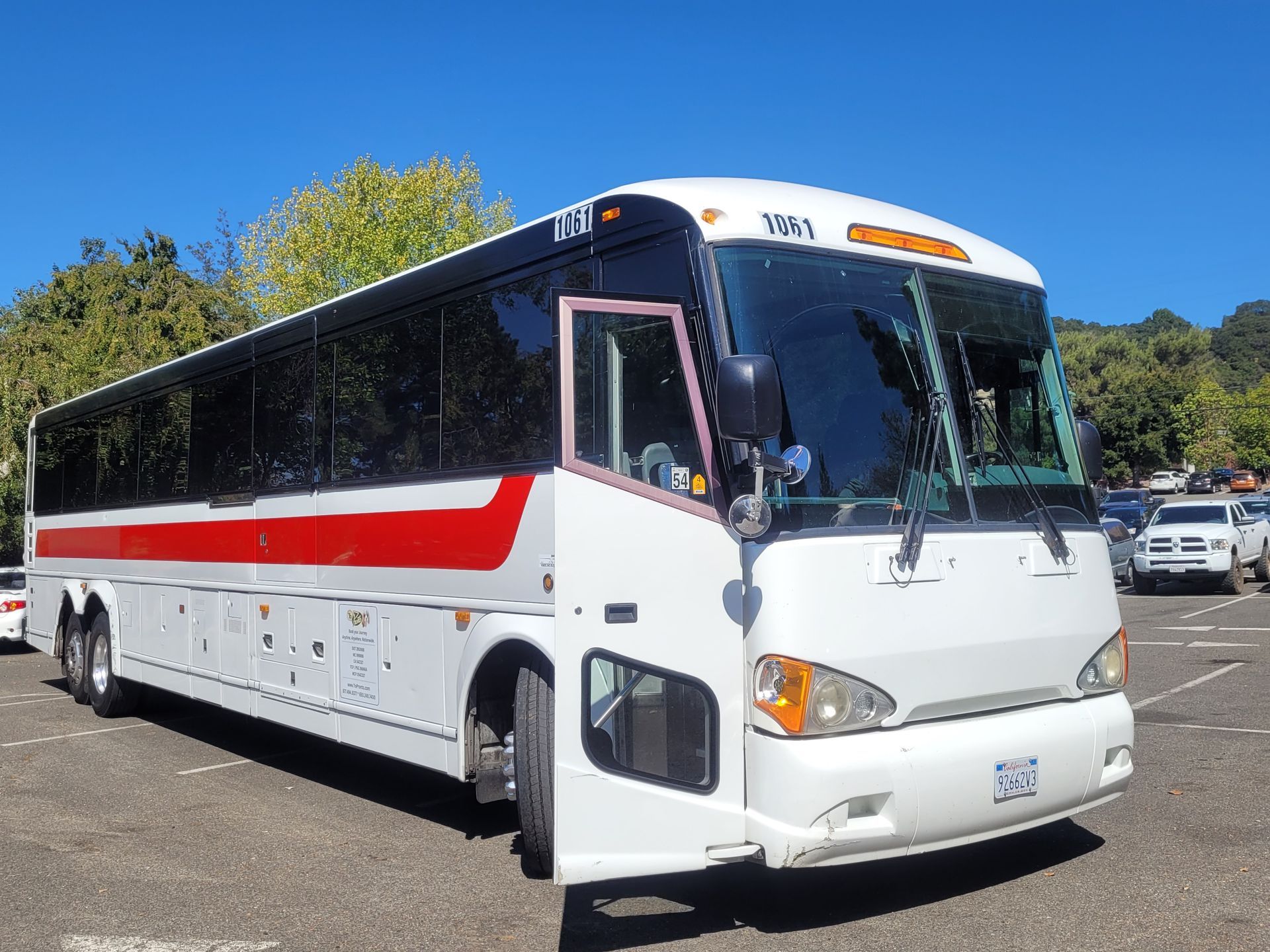 A white bus with a red stripe on the side is parked in a parking lot.