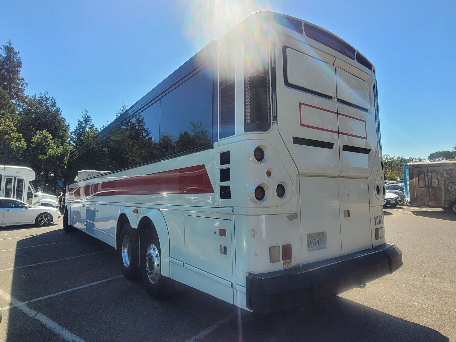 A white bus with red stripes is parked in a parking lot.