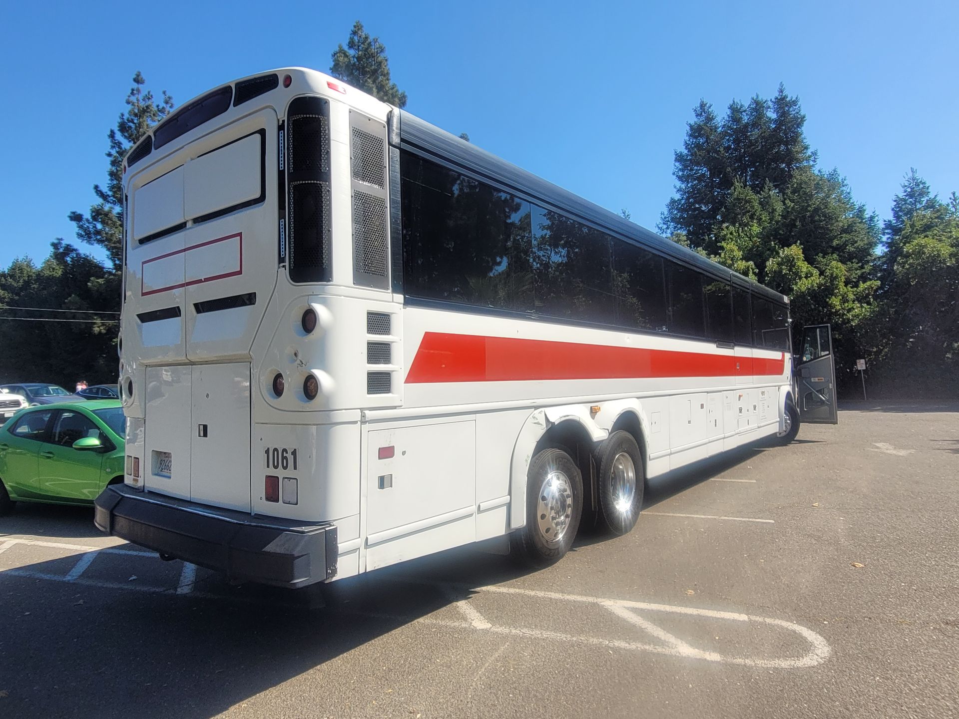 A white bus with red stripes is parked in a parking lot