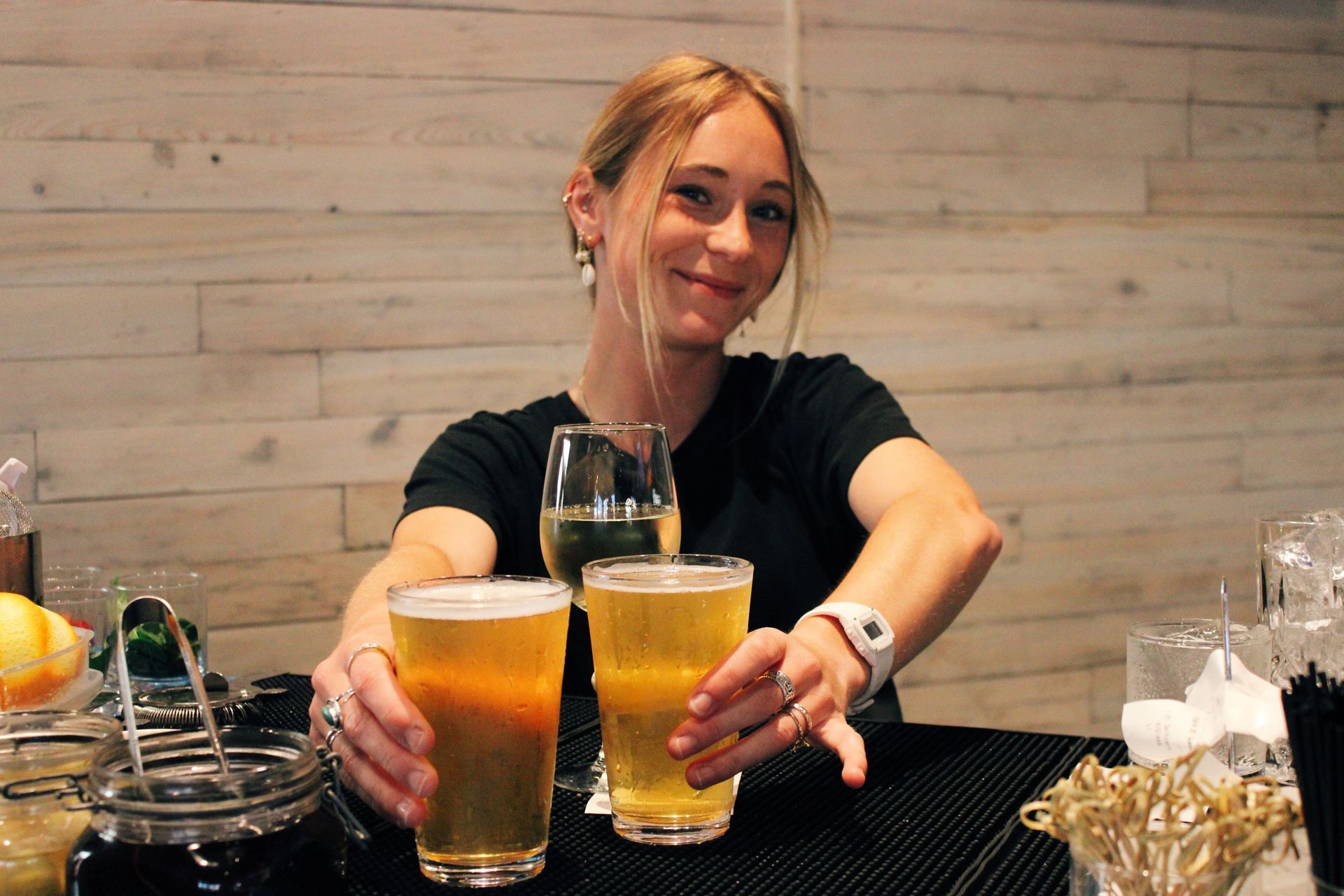 Woman at a bar clinking two beer glasses with a smiling server behind the counter