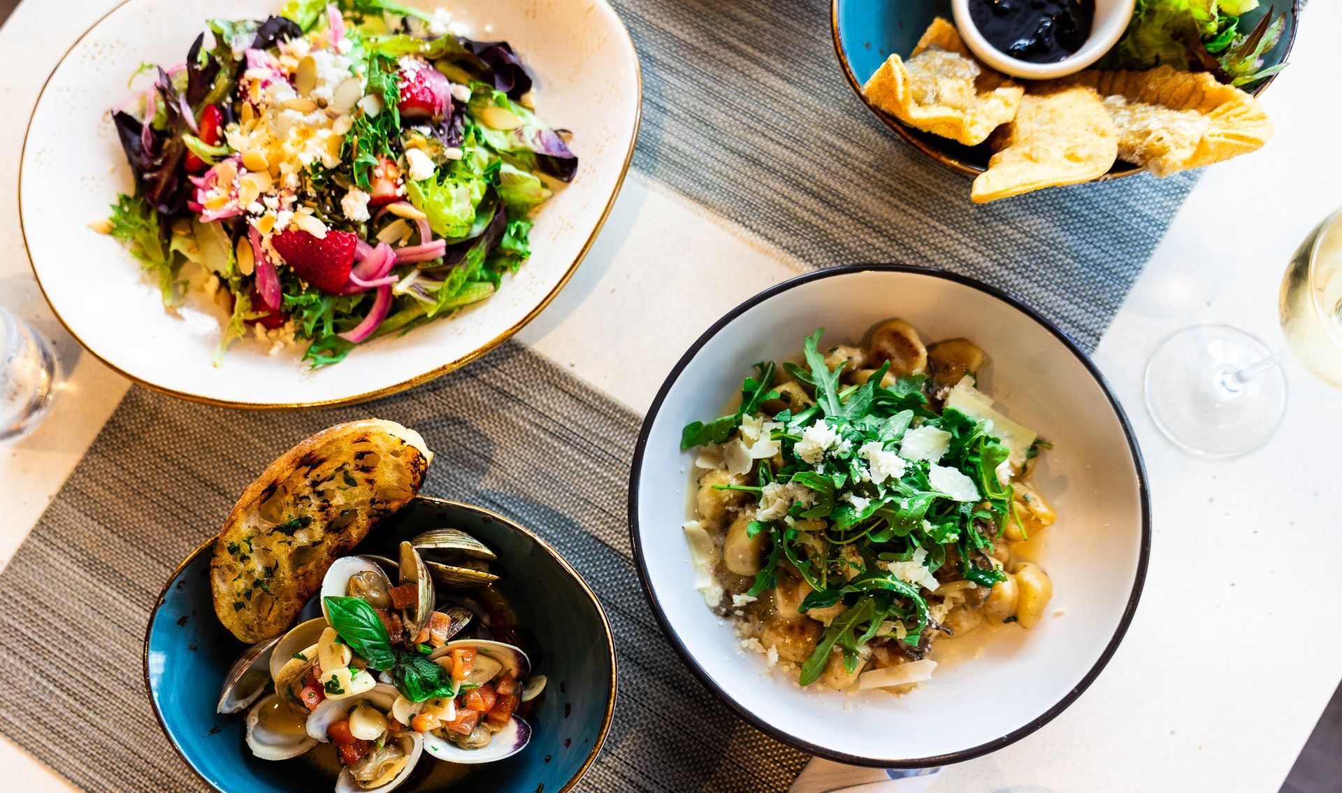 Overhead view of four plated salads and appetizers on a wooden table with a drink.