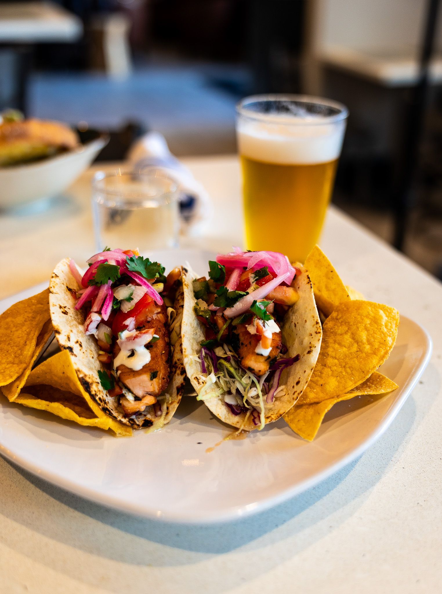 Tacos on a white plate with a glass of beer in the background