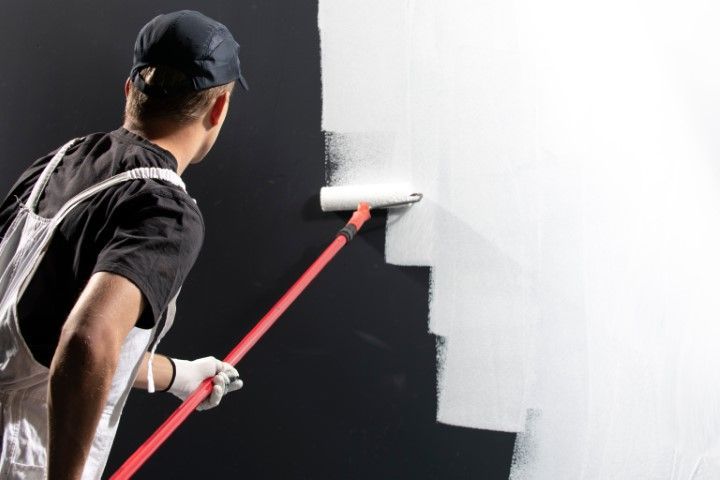 Painter rolling white paint over a black wall with a red-handled roller