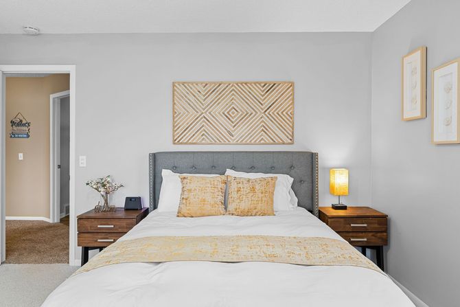 Bright bedroom with gray tufted bed, white bedding, yellow accents, nightstands, and wall art