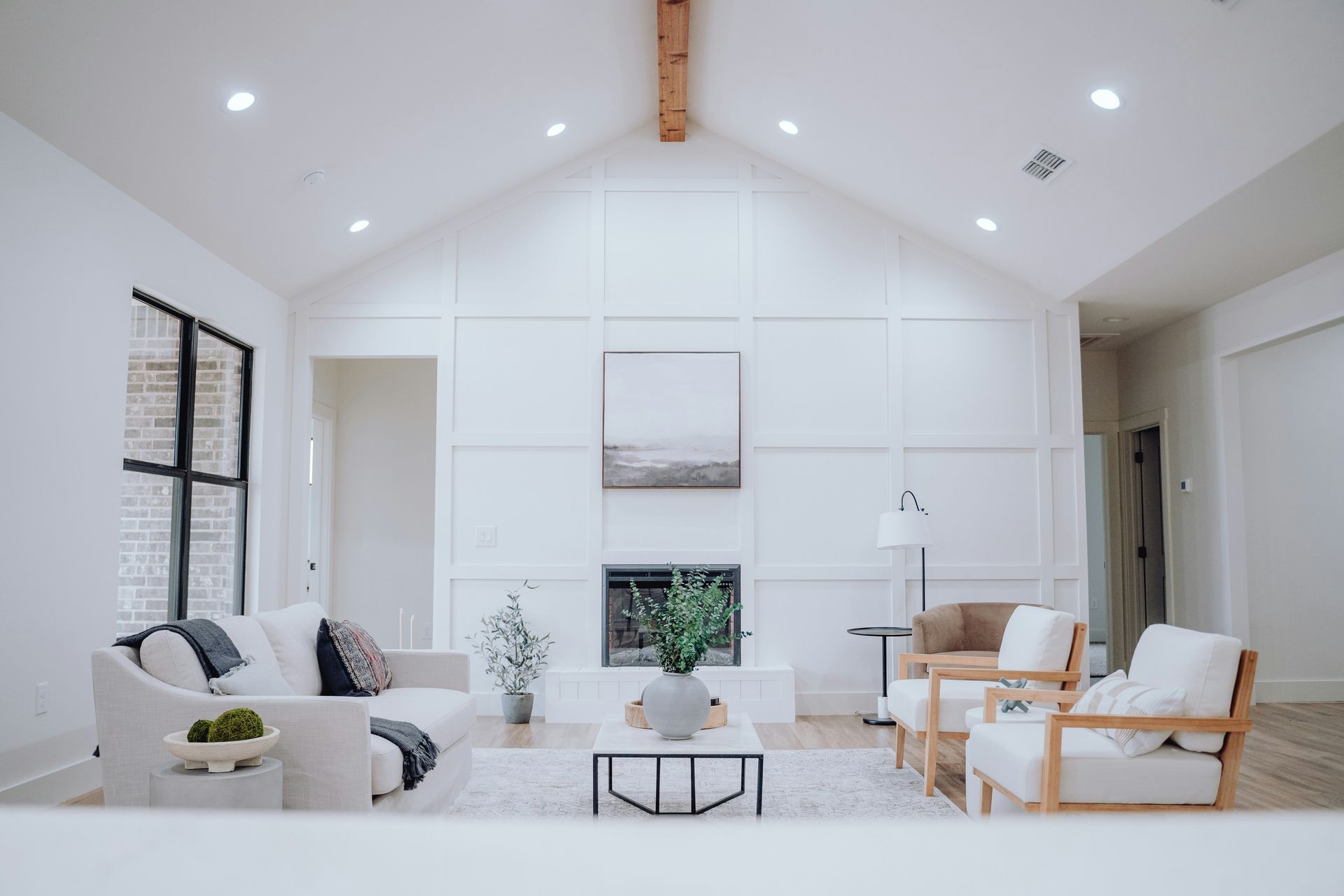 Bright white living room with vaulted ceiling, fireplace, and modern sofas around a central coffee table.