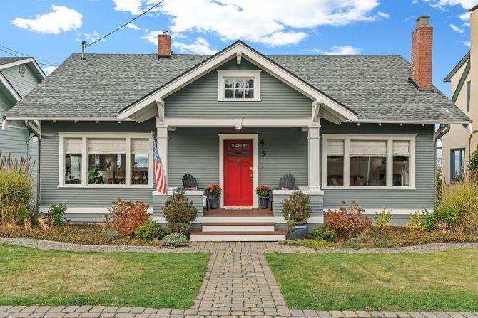 Gray house with a red front door, white trim, and a stone walkway in a sunny yard