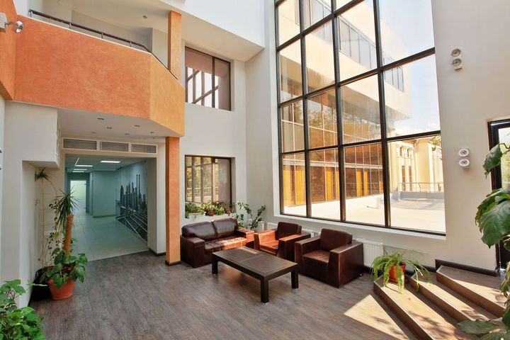 Modern indoor atrium lounge with orange walls, glass windows, and seating around a fire table
