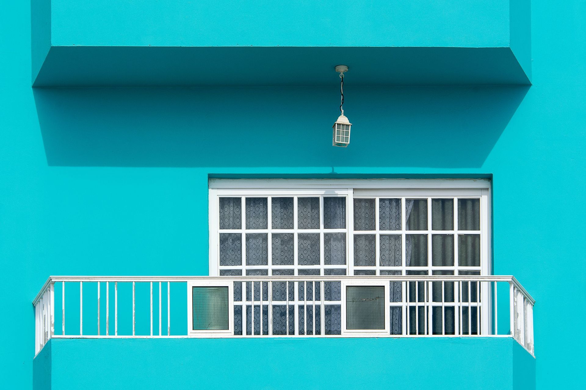 Turquoise balcony with white railing and window under a teal overhang