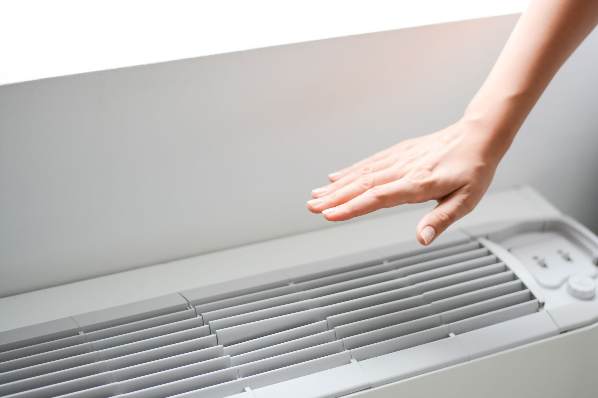 A Woman 's Hand Is Touching a White Air Conditioner.