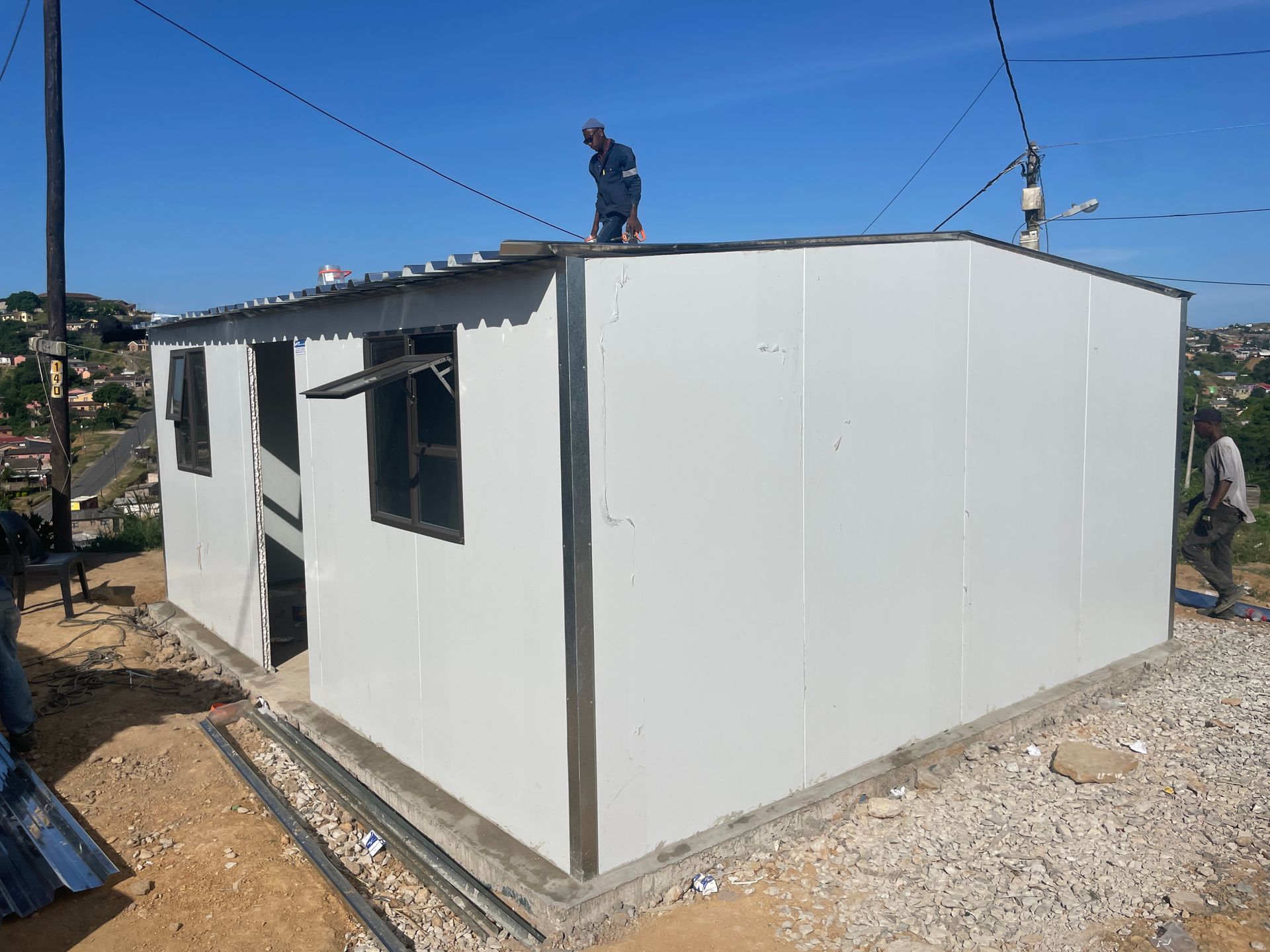 A man is standing on the roof of a small white house.