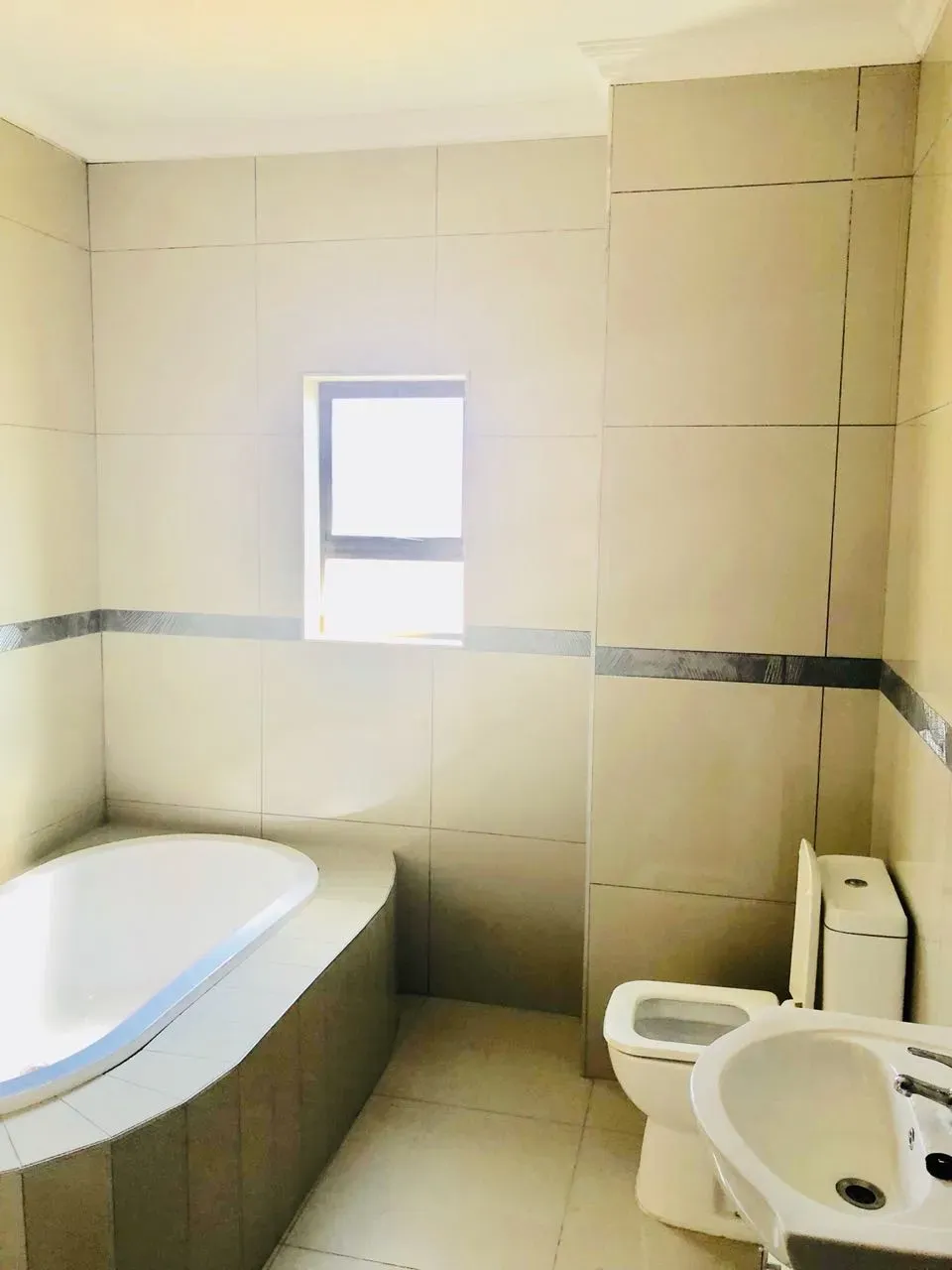 A bathroom with a tub , toilet , sink and window.