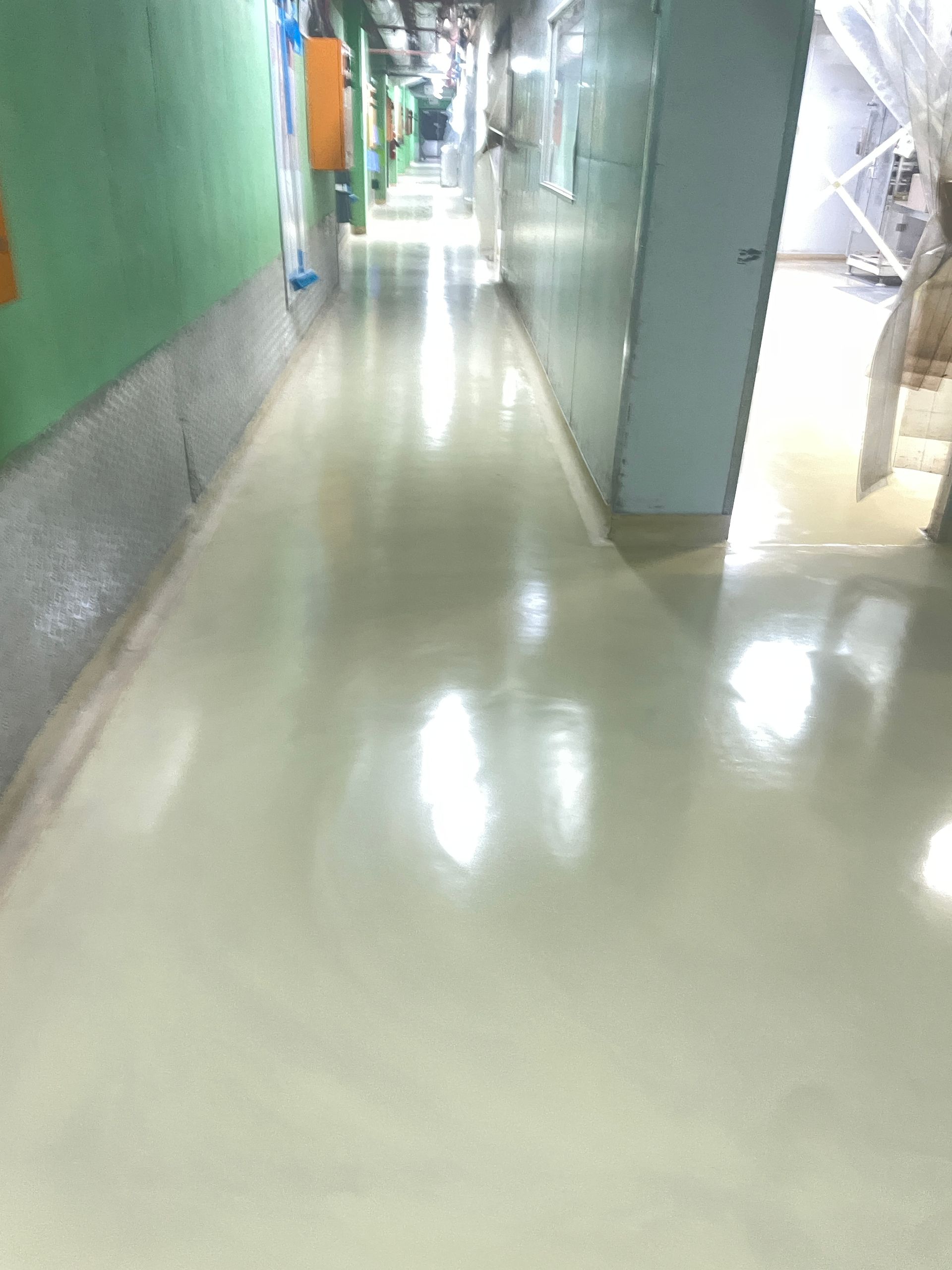 A long hallway in a building with a white floor and green walls.