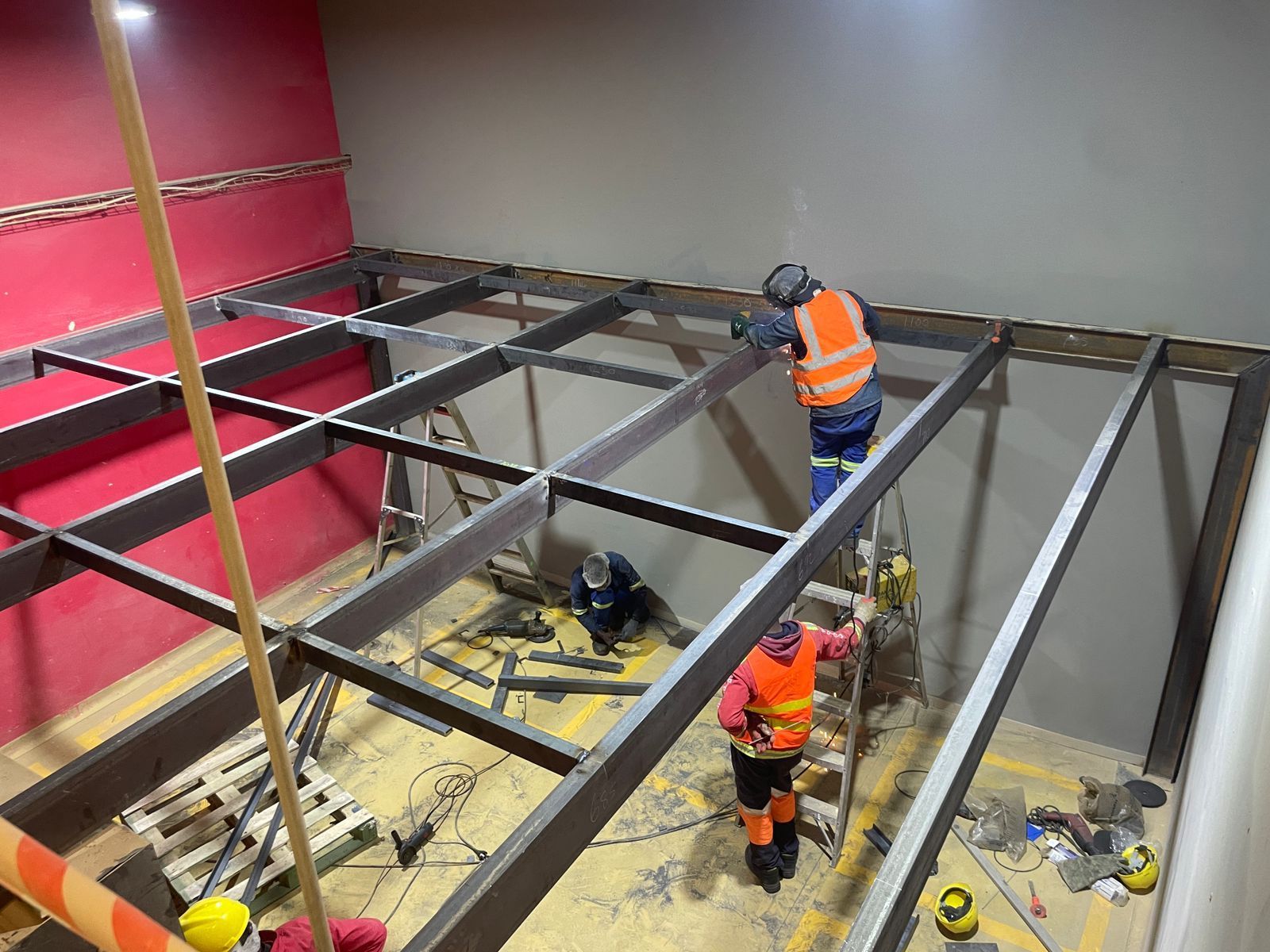 A group of construction workers are working on a metal structure in a room.