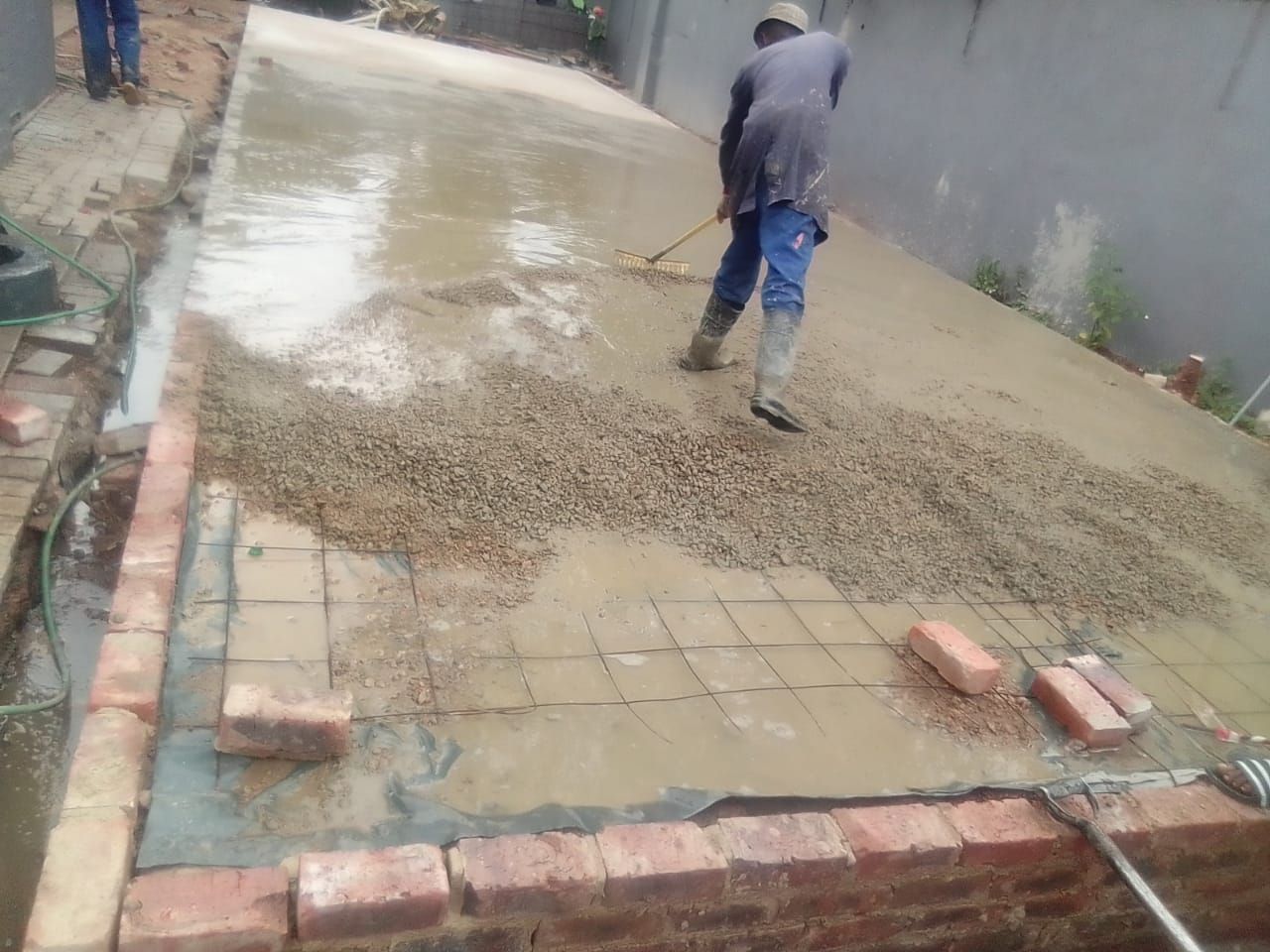 A man is spreading concrete on a brick sidewalk.