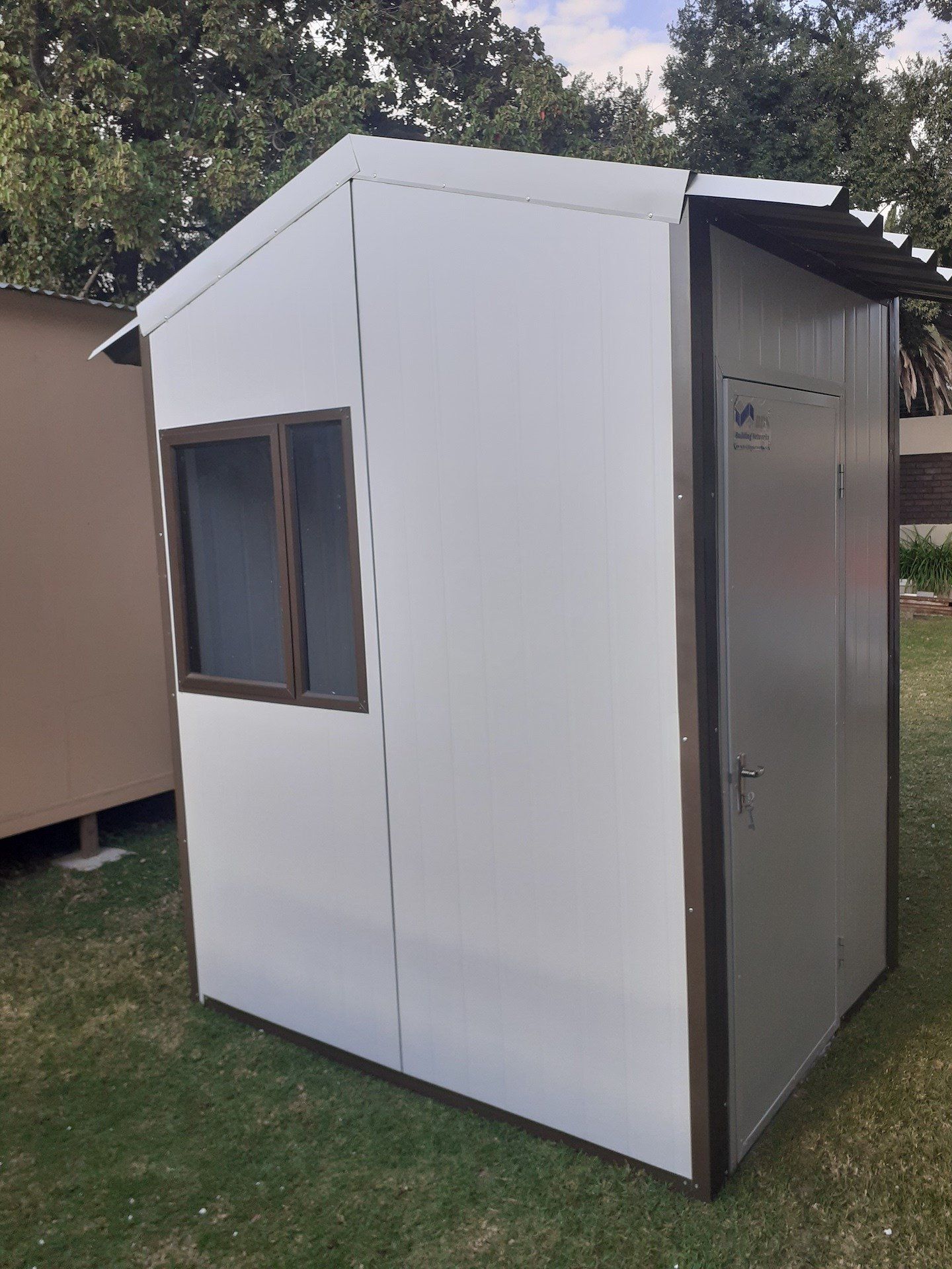 A small white shed with a window is sitting on top of a lush green field.