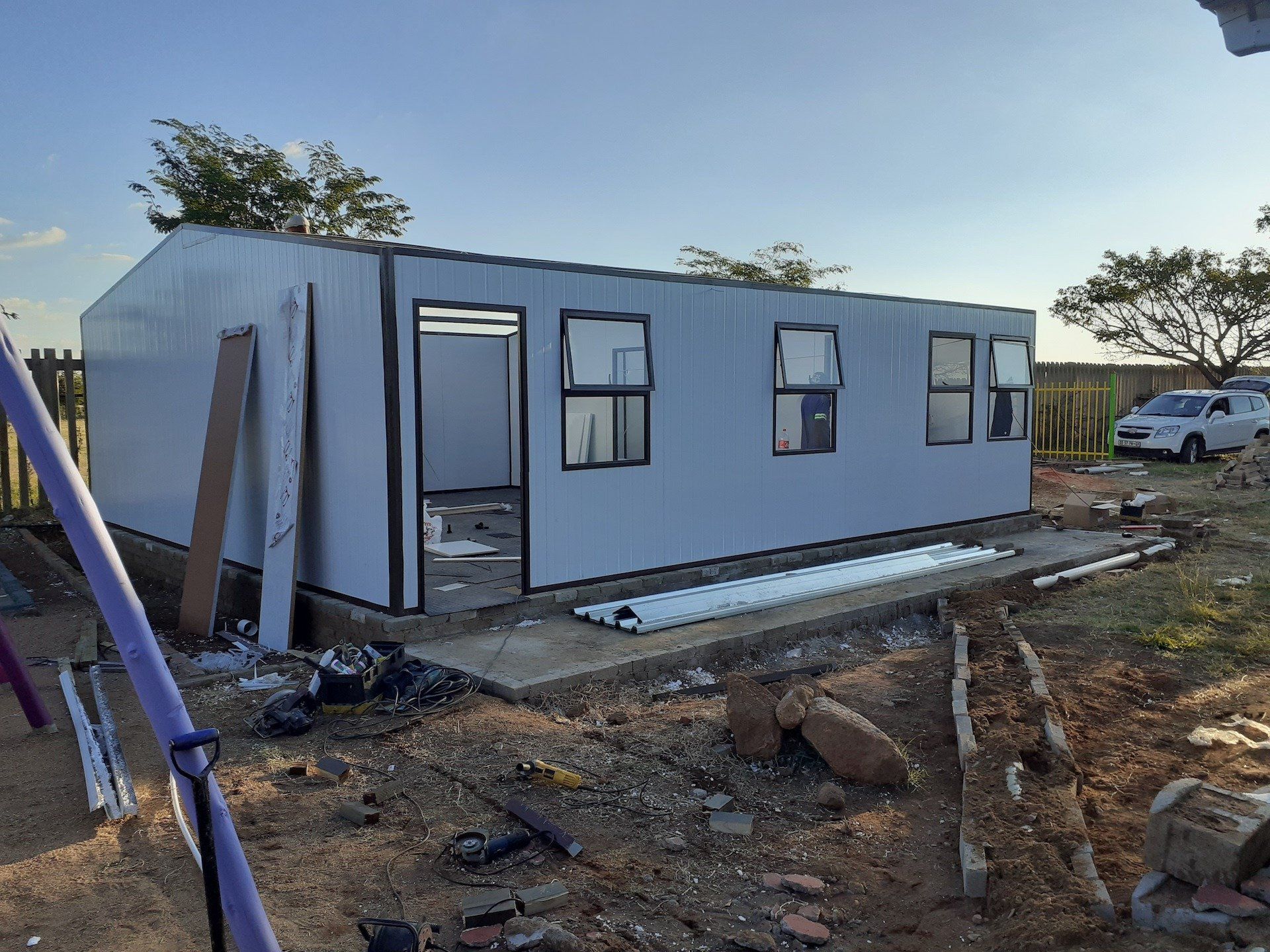 A small white house is being built in a dirt field.
