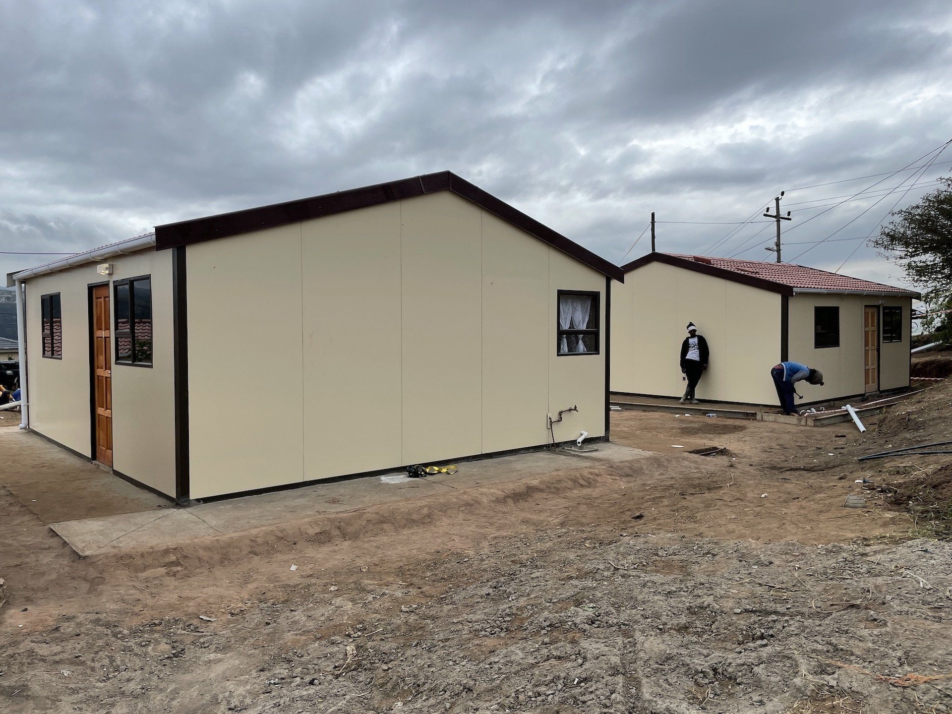 Two small houses are being built in a dirt field.