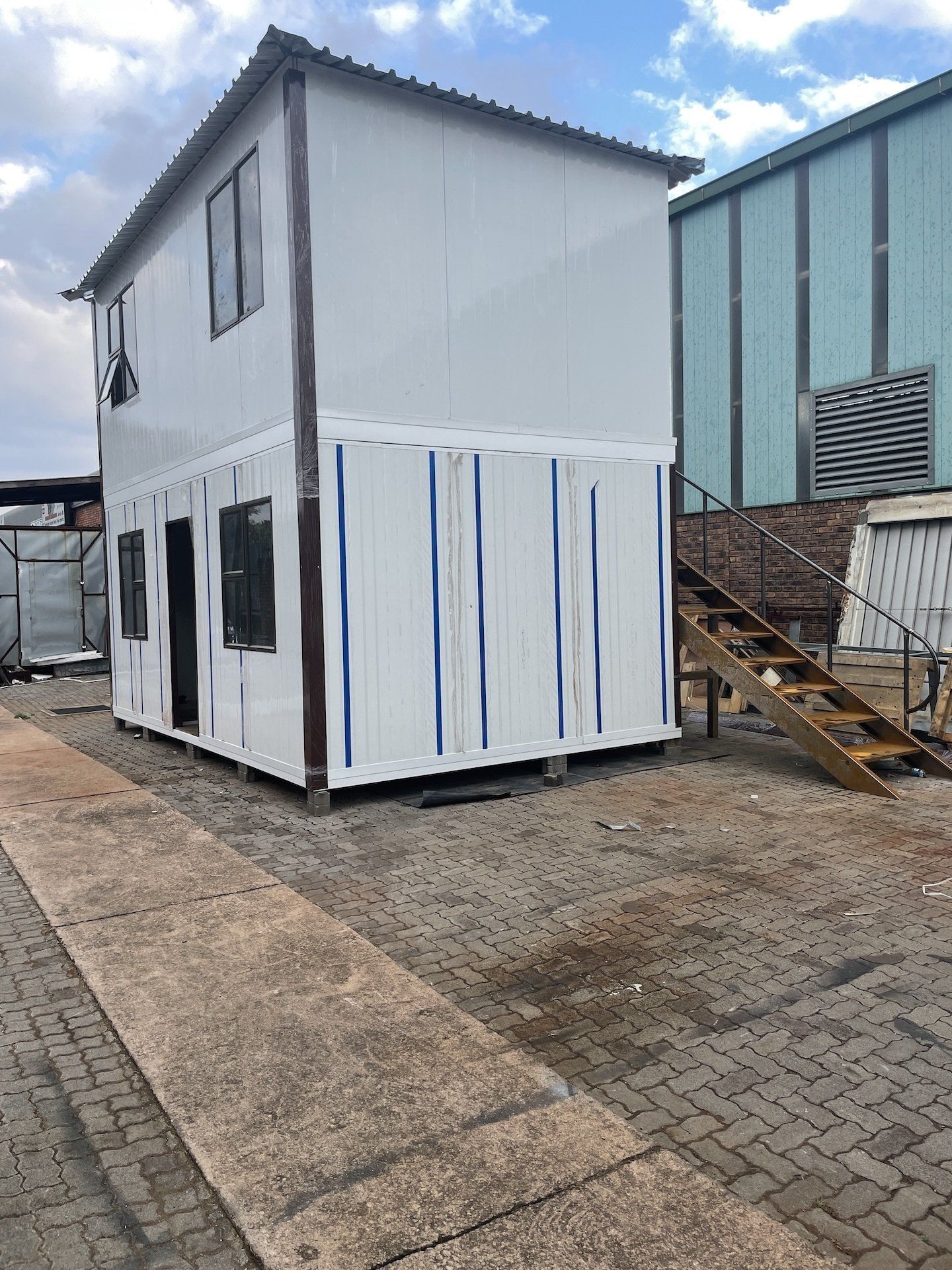 A white house with stairs leading up to it is sitting in a parking lot next to a building.