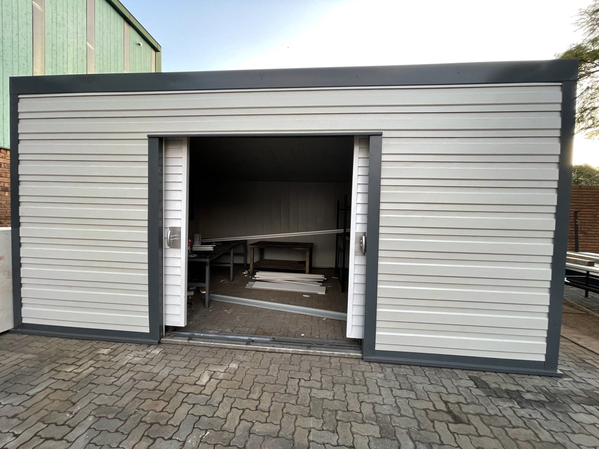 A white garage with a sliding door is sitting on a brick driveway.