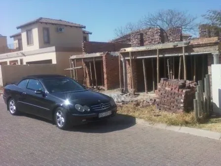 A black car is parked in front of a house under construction