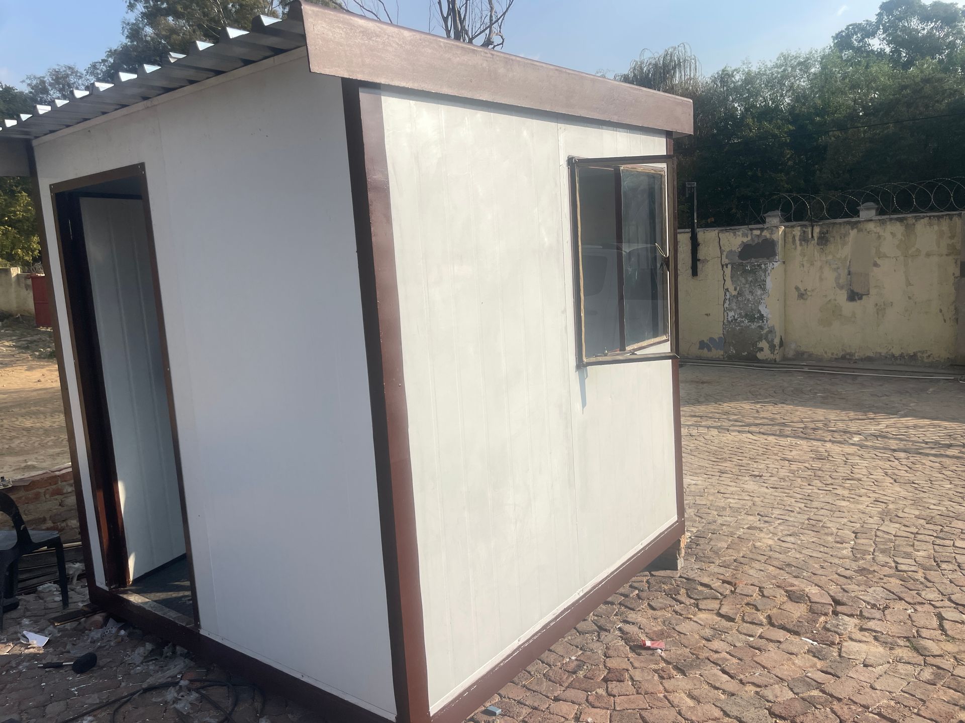 A small white building with a window is sitting on top of a brick driveway.