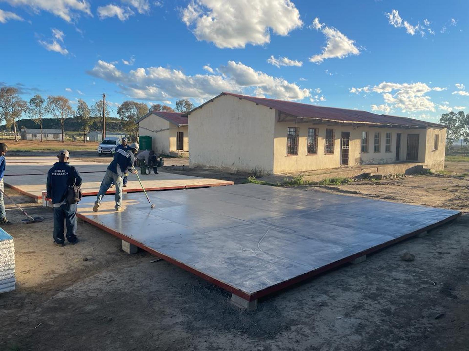 A group of people are working on a large piece of wood in front of a building.