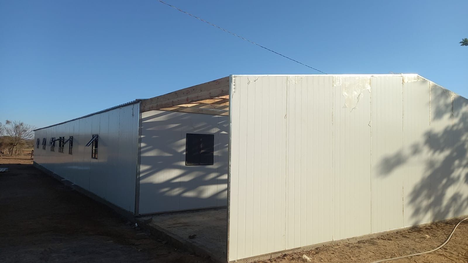 A large white building is being built in the middle of a dirt field.