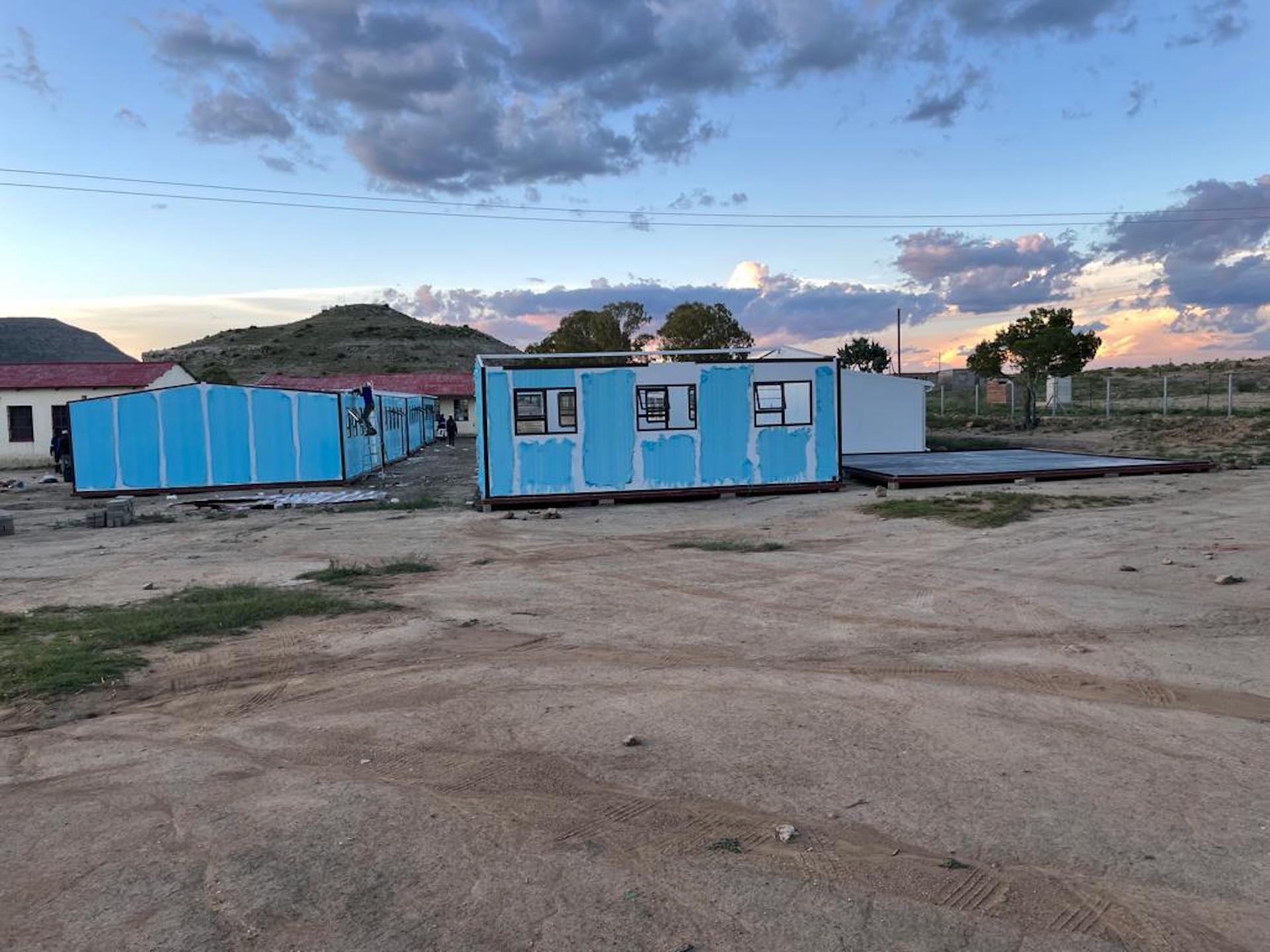 A row of blue containers are sitting in a dirt field.