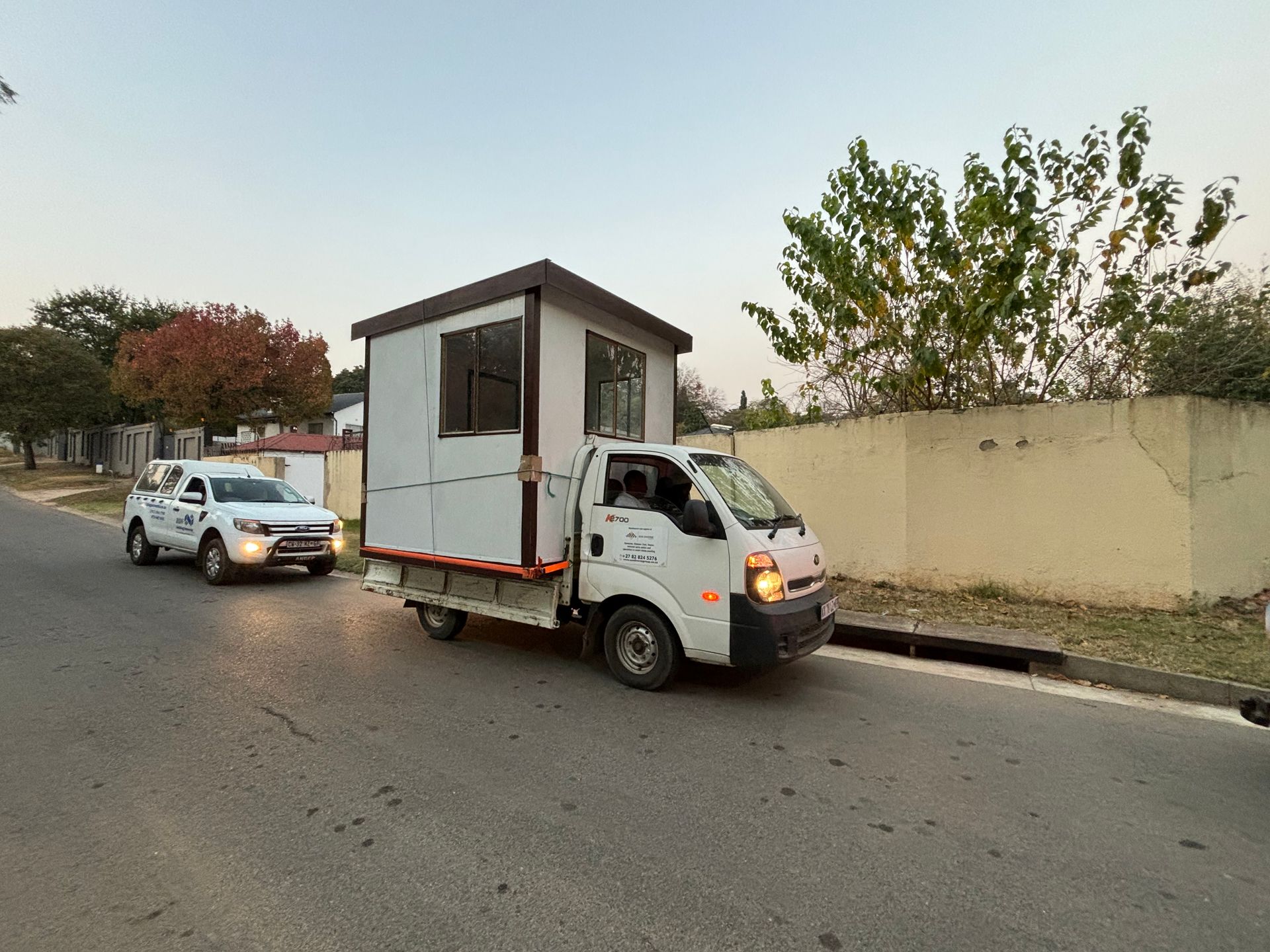 A white truck is towing a small house down a street.
