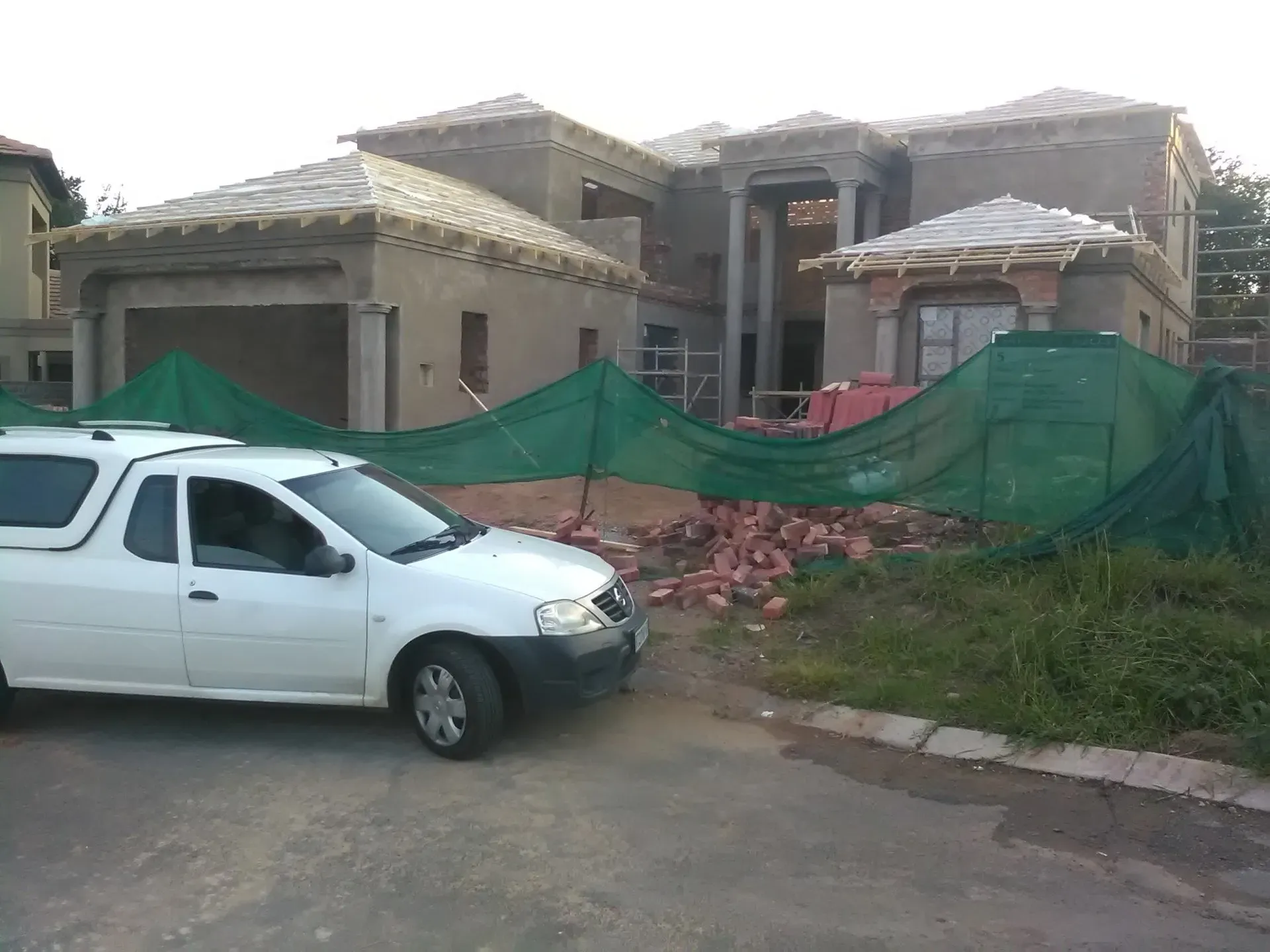 A white truck is parked in front of a house under construction.