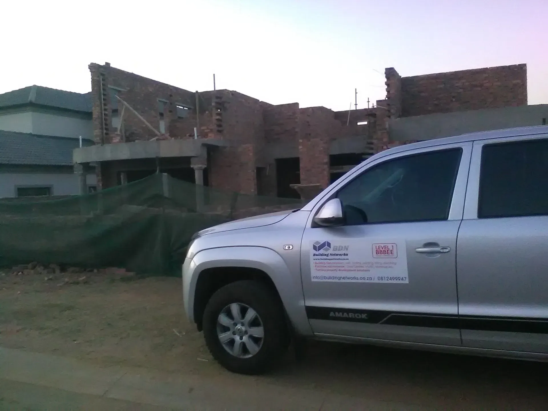 A silver truck is parked in front of a building under construction