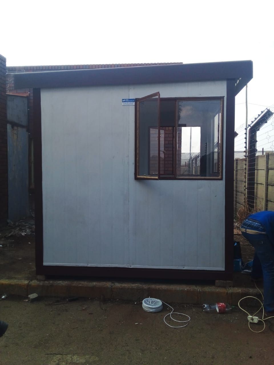 A small building with a window and a fence in the background