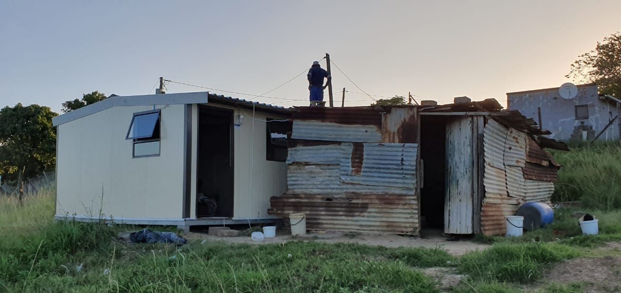 A man is standing on the roof of a small house.