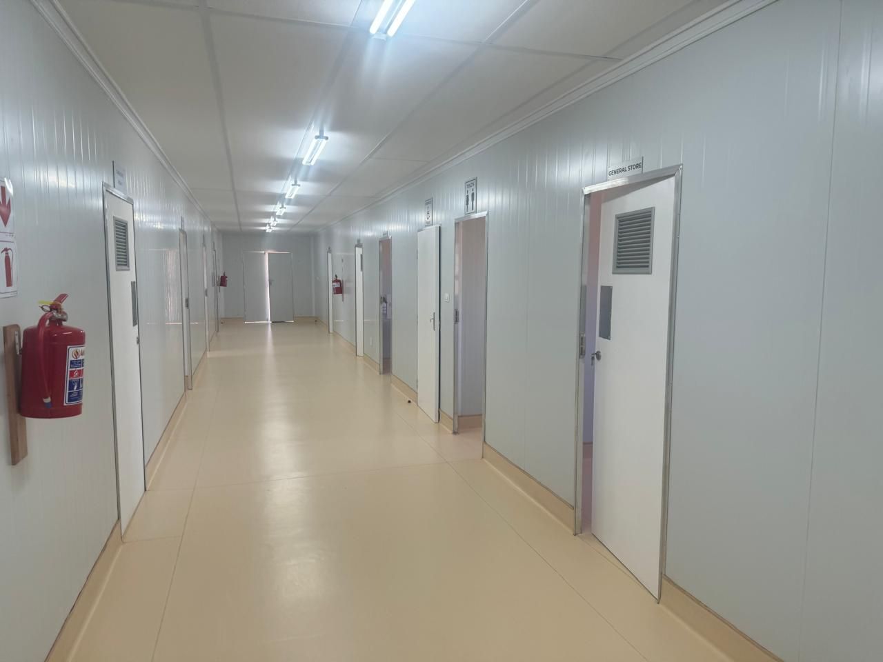 A long hallway in a hospital with a fire extinguisher on the wall.