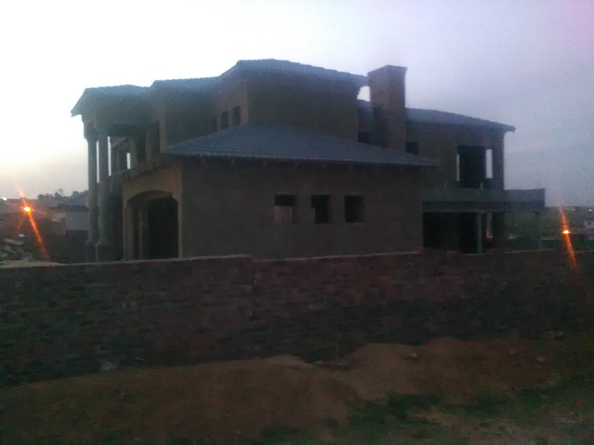 A large house under construction with a brick wall surrounding it
