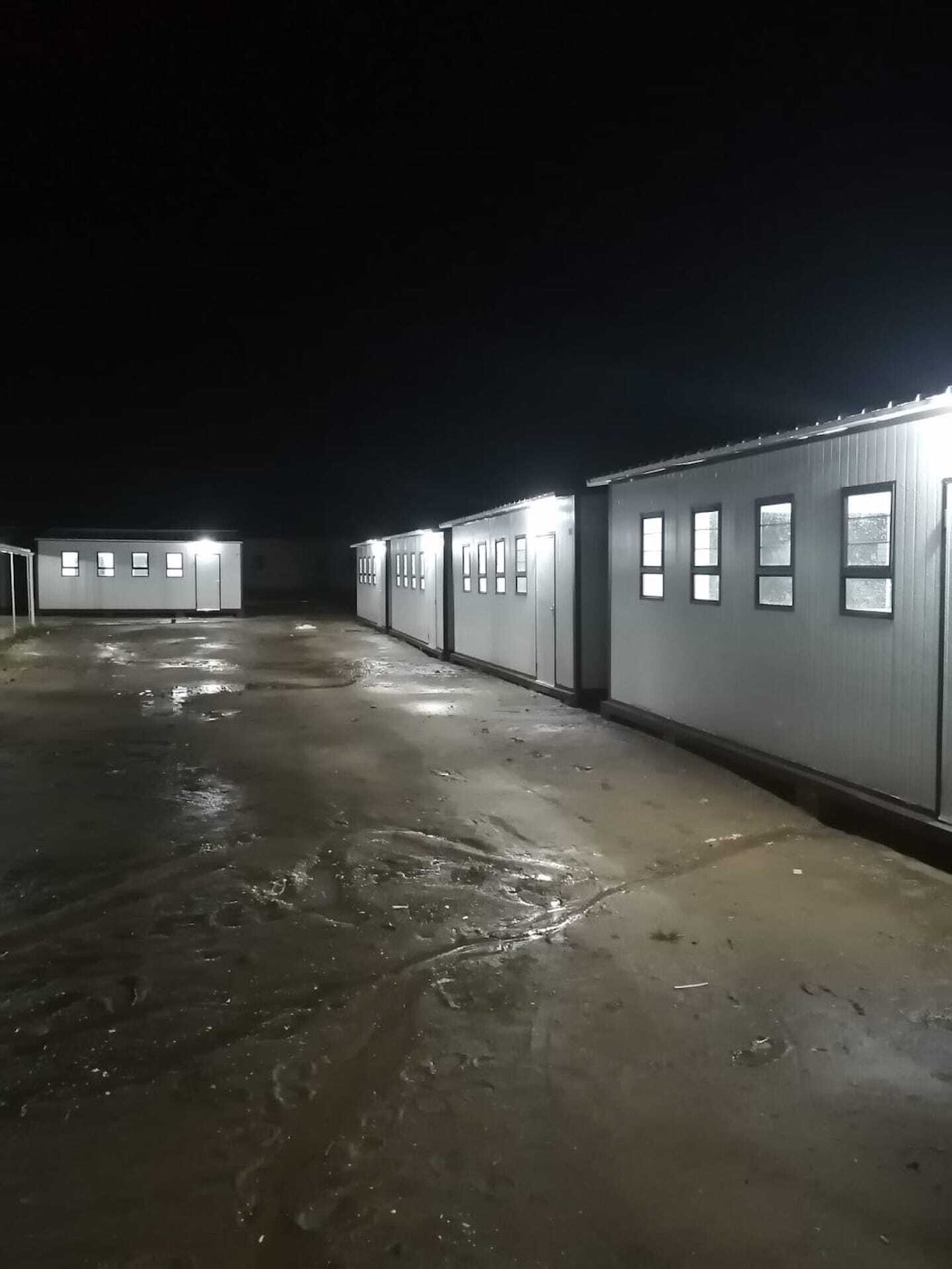 A row of buildings are lit up at night in a parking lot.