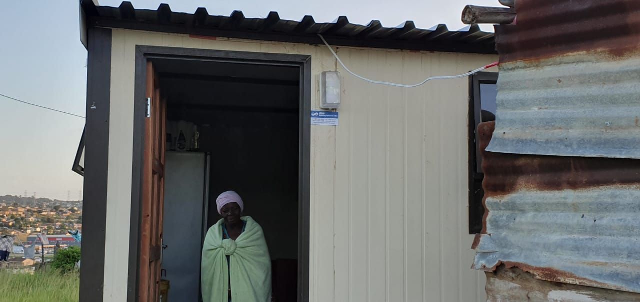 A woman is standing in the doorway of a small house.